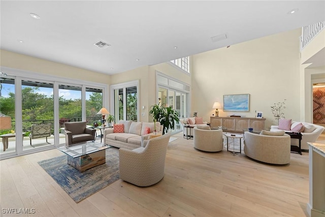 living room with a towering ceiling, light hardwood / wood-style flooring, and a healthy amount of sunlight