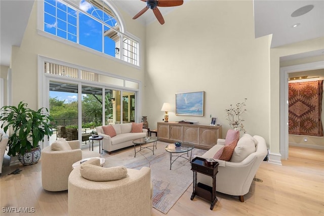 living room featuring ceiling fan, a towering ceiling, and light wood-type flooring