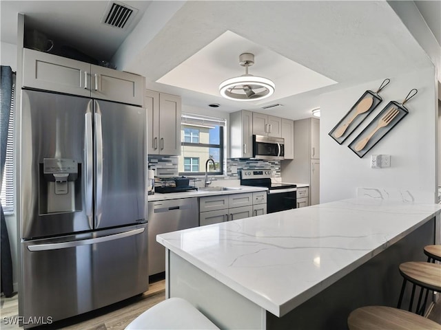 kitchen with sink, gray cabinetry, a kitchen bar, light stone counters, and stainless steel appliances