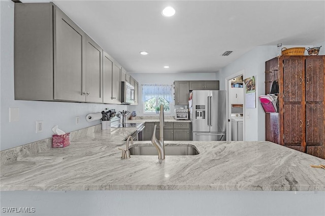 kitchen with washer / dryer, sink, gray cabinetry, light stone counters, and appliances with stainless steel finishes