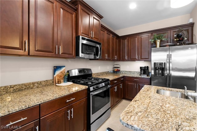 kitchen featuring light stone countertops, light tile patterned floors, appliances with stainless steel finishes, and a sink