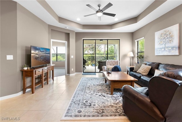 living area featuring light tile patterned floors, a raised ceiling, a wealth of natural light, and baseboards