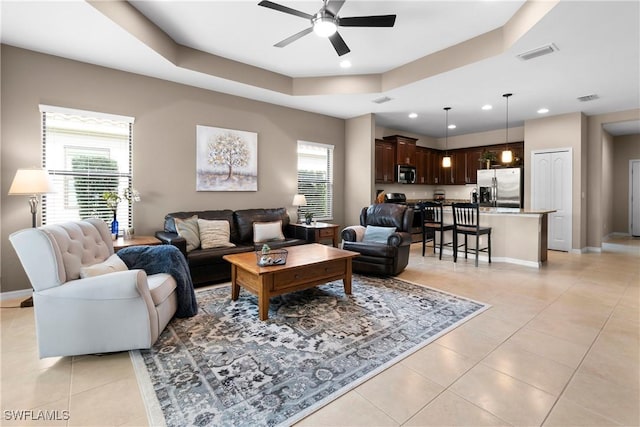 living area with a wealth of natural light, a tray ceiling, visible vents, and light tile patterned floors