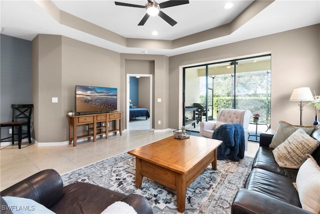 living area featuring a raised ceiling, ceiling fan, baseboards, and tile patterned floors