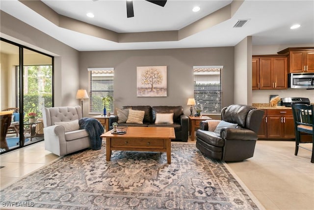 living room with light tile patterned floors, visible vents, ceiling fan, a tray ceiling, and recessed lighting