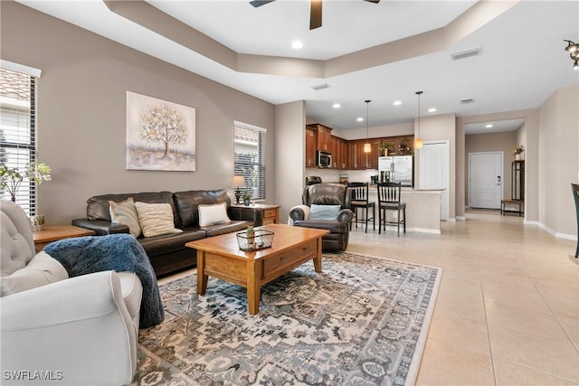 living area with a raised ceiling, visible vents, a ceiling fan, light tile patterned flooring, and baseboards