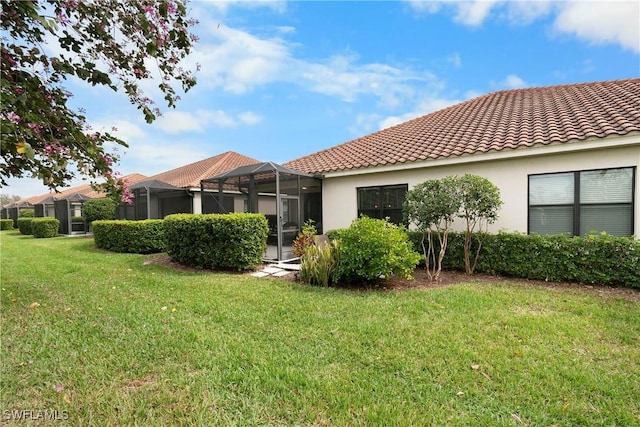 back of house with a lanai, a tile roof, a yard, and stucco siding