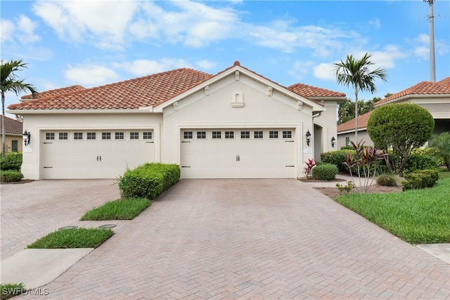 mediterranean / spanish home with a garage, a tiled roof, decorative driveway, and stucco siding