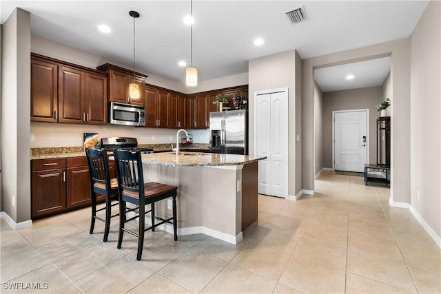 kitchen featuring visible vents, an island with sink, appliances with stainless steel finishes, light stone countertops, and a sink