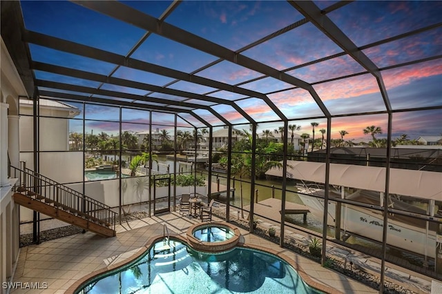 pool at dusk featuring an in ground hot tub, a patio area, and glass enclosure