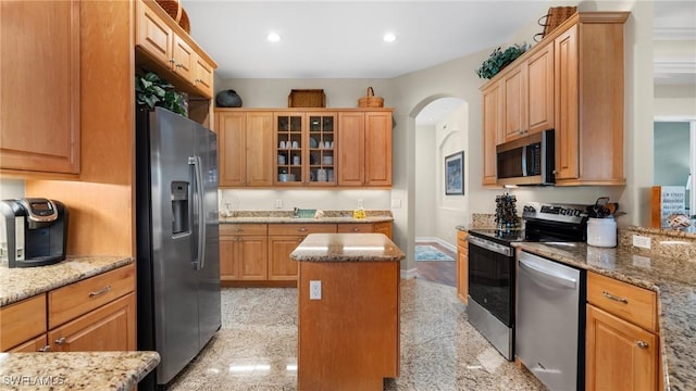 kitchen featuring glass insert cabinets, light stone countertops, a kitchen island, and appliances with stainless steel finishes