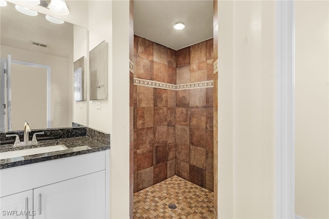 bathroom with visible vents, a tile shower, and vanity