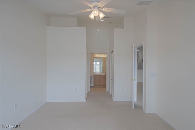 unfurnished bedroom featuring baseboards, visible vents, connected bathroom, light colored carpet, and a towering ceiling