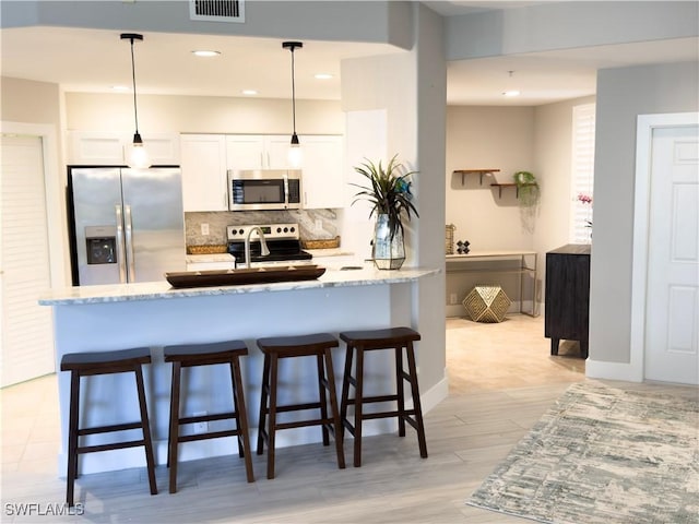 kitchen featuring a breakfast bar, stainless steel appliances, visible vents, decorative backsplash, and light stone countertops