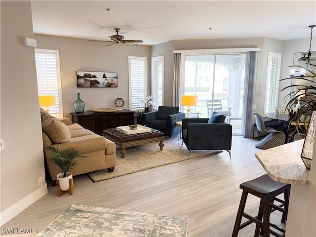 living room with light wood-type flooring, a healthy amount of sunlight, baseboards, and ceiling fan with notable chandelier