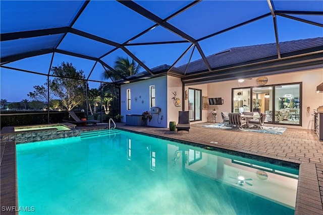 pool at dusk with an in ground hot tub, a patio, and glass enclosure