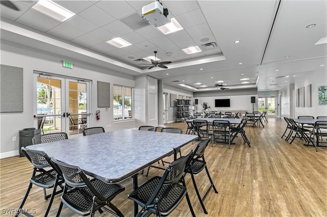 dining area featuring a raised ceiling, a healthy amount of sunlight, light hardwood / wood-style floors, and french doors