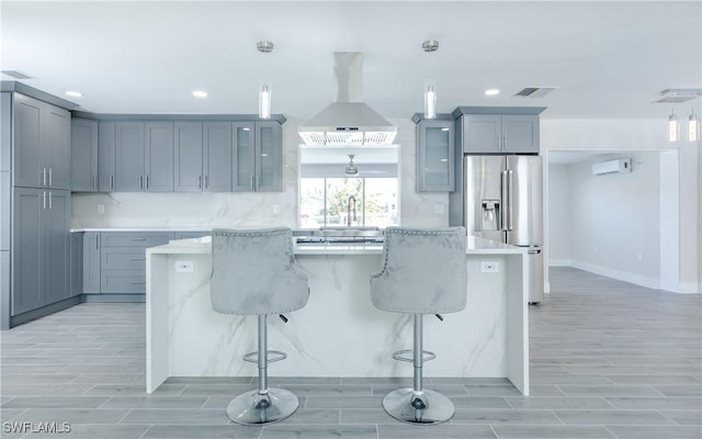 kitchen with a breakfast bar, a center island, stainless steel fridge with ice dispenser, hanging light fixtures, and island exhaust hood