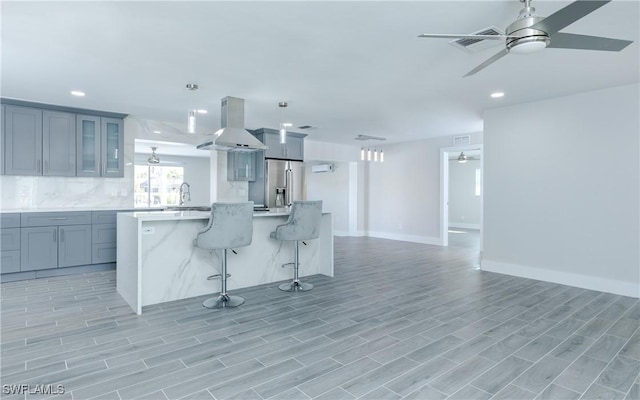 kitchen featuring a breakfast bar area, high end refrigerator, gray cabinets, ceiling fan, and range hood