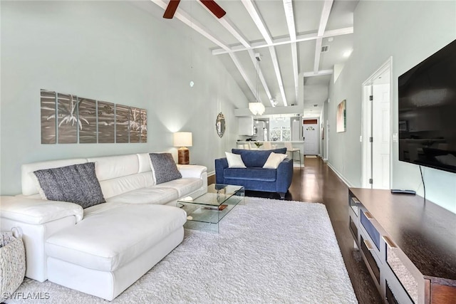 living room with dark wood-type flooring, ceiling fan, beam ceiling, and a high ceiling