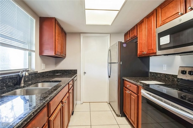 kitchen with light tile patterned flooring, appliances with stainless steel finishes, sink, and dark stone countertops