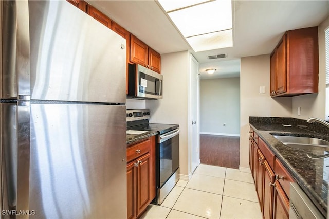 kitchen featuring sink, light tile patterned flooring, dark stone counters, and appliances with stainless steel finishes