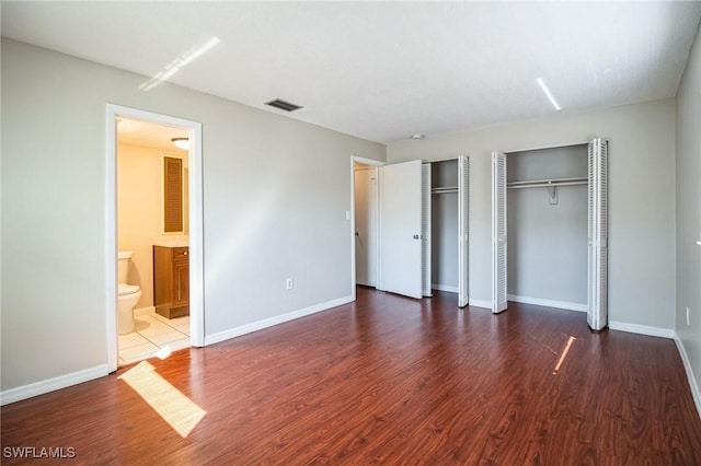 unfurnished bedroom with ensuite bathroom, dark hardwood / wood-style floors, and two closets