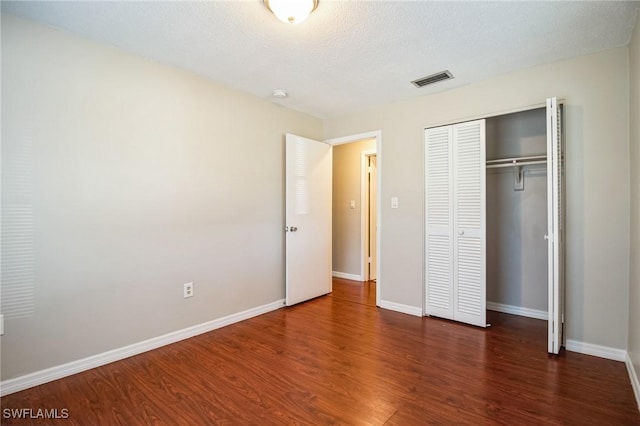 unfurnished bedroom with dark hardwood / wood-style floors, a textured ceiling, and a closet