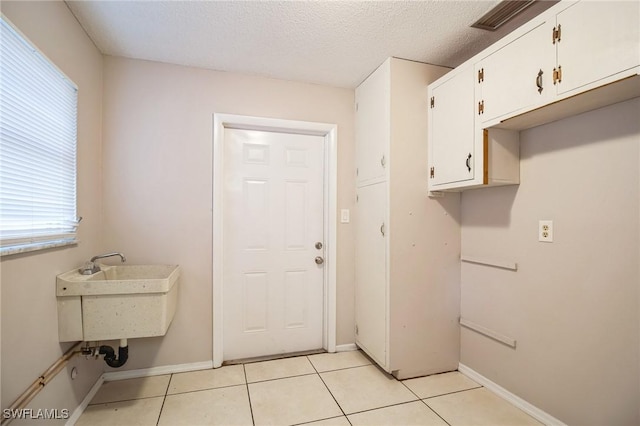 laundry room with light tile patterned floors, sink, cabinets, and a textured ceiling