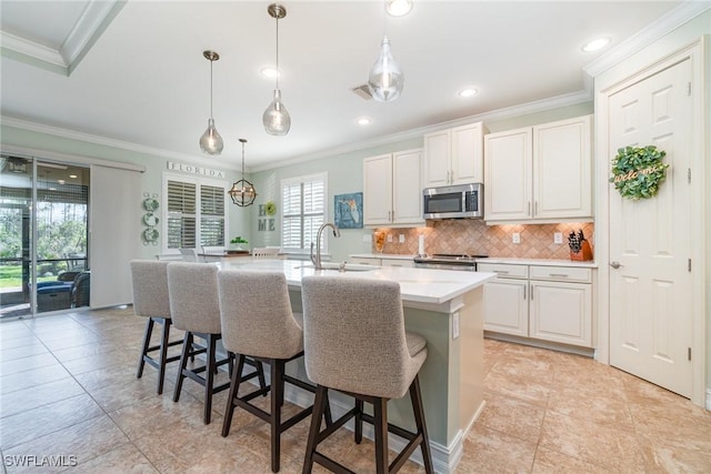 kitchen featuring appliances with stainless steel finishes, an island with sink, white cabinets, decorative backsplash, and hanging light fixtures