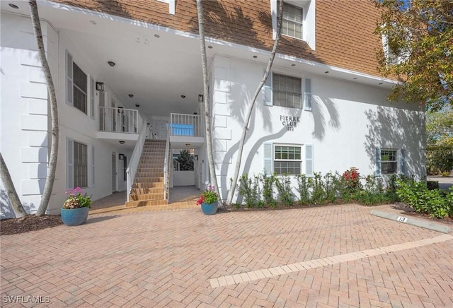 exterior space featuring a shingled roof, mansard roof, and stucco siding