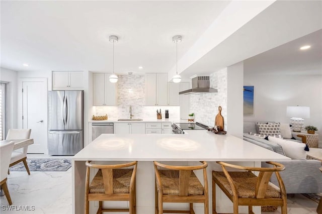 kitchen featuring stainless steel appliances, a sink, marble finish floor, wall chimney range hood, and tasteful backsplash