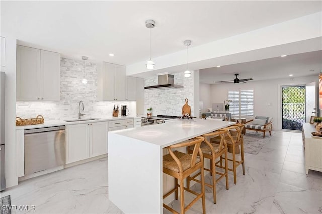 kitchen with stainless steel appliances, a sink, marble finish floor, backsplash, and wall chimney exhaust hood