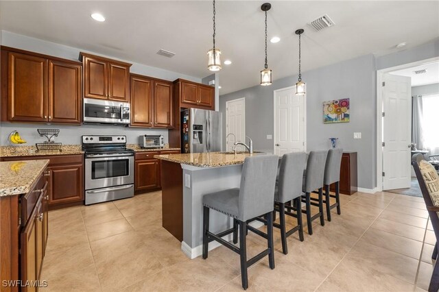 kitchen with a center island with sink, light tile patterned floors, appliances with stainless steel finishes, a sink, and a kitchen bar