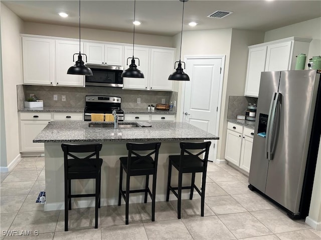 kitchen featuring hanging light fixtures, appliances with stainless steel finishes, light stone countertops, a kitchen island with sink, and white cabinets