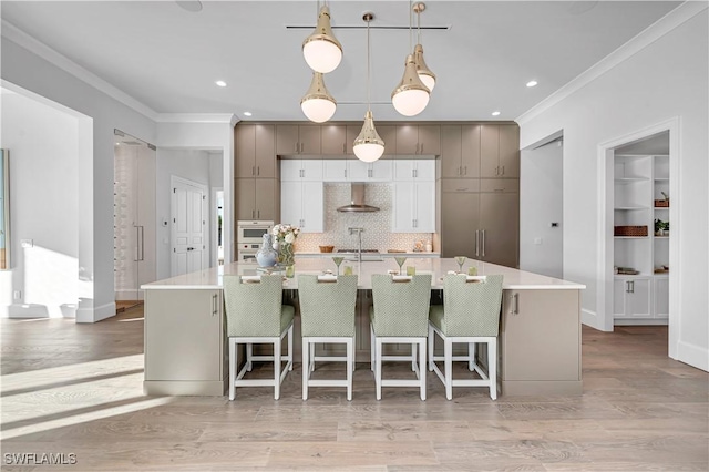 kitchen featuring pendant lighting, a kitchen bar, ornamental molding, wall chimney exhaust hood, and a spacious island