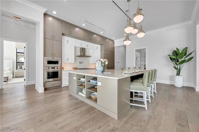 kitchen featuring pendant lighting, light hardwood / wood-style flooring, ornamental molding, and a large island with sink