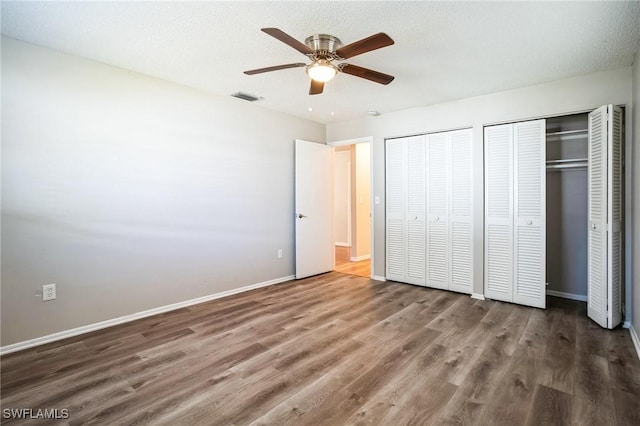 unfurnished bedroom featuring two closets, dark wood-type flooring, a textured ceiling, and ceiling fan