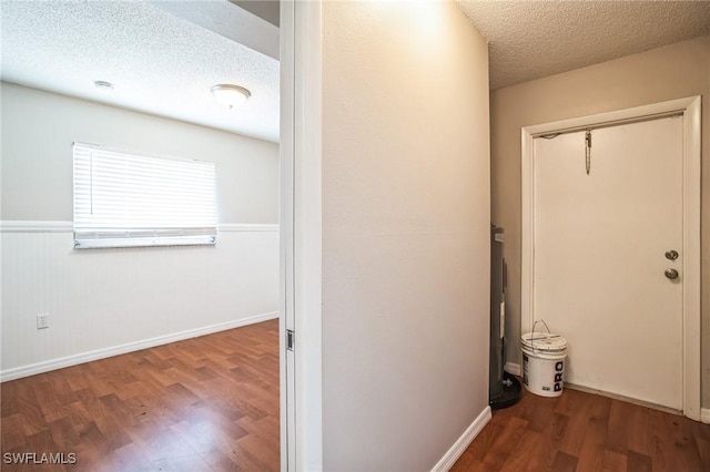 hallway featuring electric water heater, dark wood-type flooring, and a textured ceiling