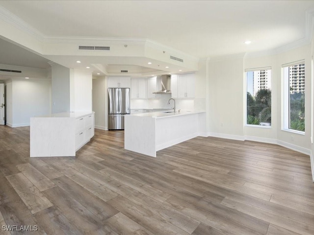 kitchen with stainless steel fridge, white cabinetry, kitchen peninsula, wall chimney exhaust hood, and light wood-type flooring