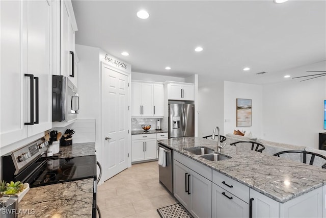 kitchen featuring an island with sink, stainless steel appliances, light stone countertops, sink, and white cabinets