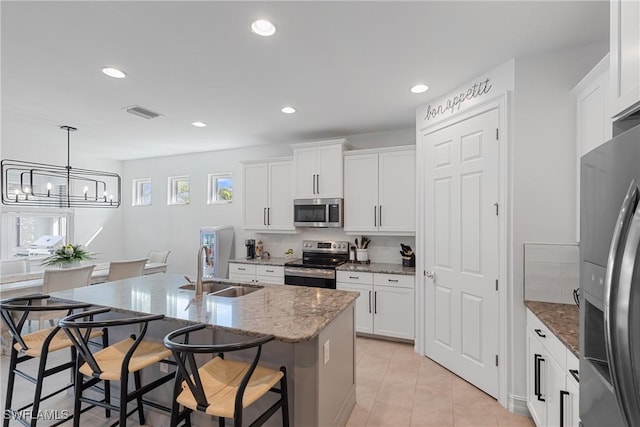 kitchen featuring appliances with stainless steel finishes, light stone countertops, sink, white cabinetry, and a kitchen island with sink