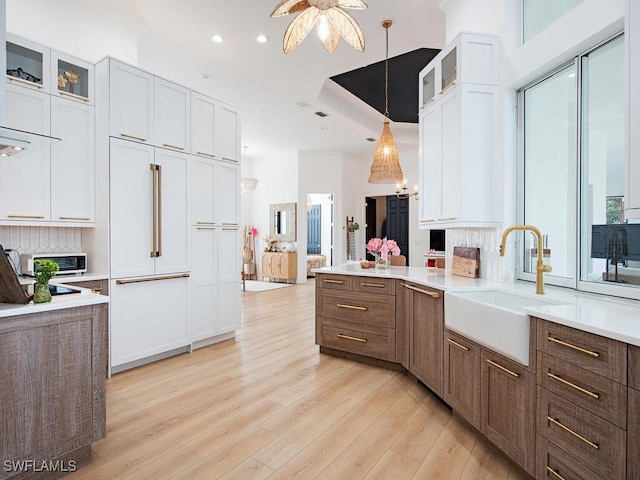 kitchen with sink, hanging light fixtures, white cabinets, and light hardwood / wood-style floors