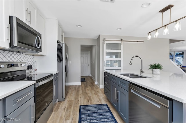 kitchen with stainless steel appliances, a barn door, sink, and white cabinets