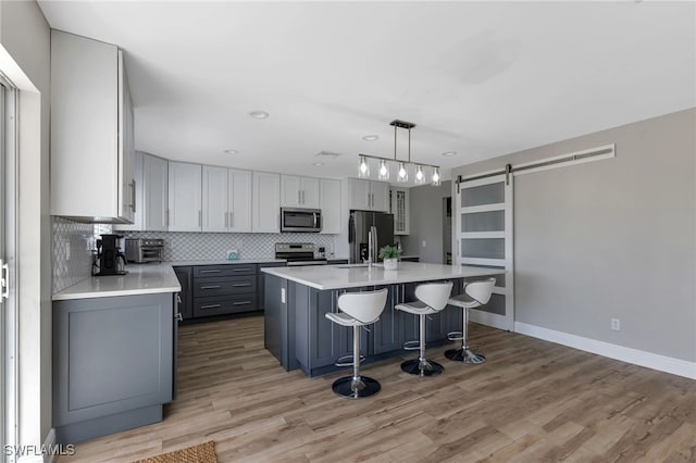 kitchen with gray cabinets, pendant lighting, stainless steel appliances, a barn door, and a center island with sink