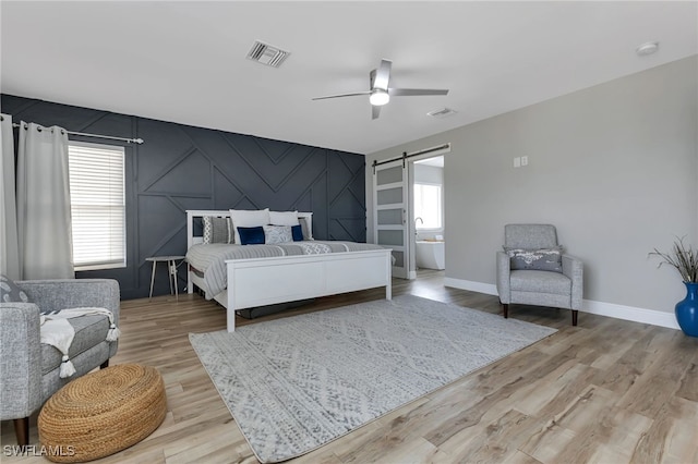 bedroom with multiple windows, a barn door, ceiling fan, and light hardwood / wood-style flooring