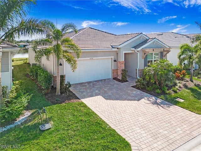 view of front of house featuring an attached garage, a water view, decorative driveway, stucco siding, and a front yard