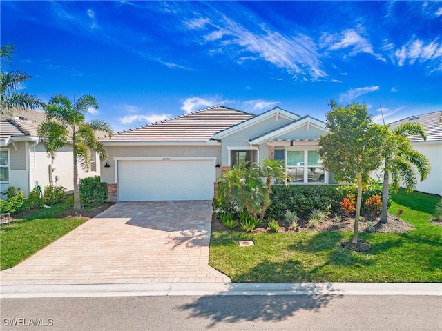 ranch-style home featuring decorative driveway, stucco siding, an attached garage, a front yard, and a tiled roof