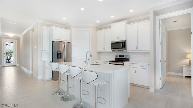 kitchen featuring a center island with sink, white cabinetry, stainless steel appliances, and light countertops