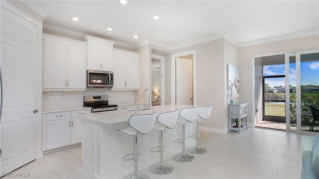 kitchen with stainless steel appliances, light countertops, a kitchen island with sink, and white cabinetry